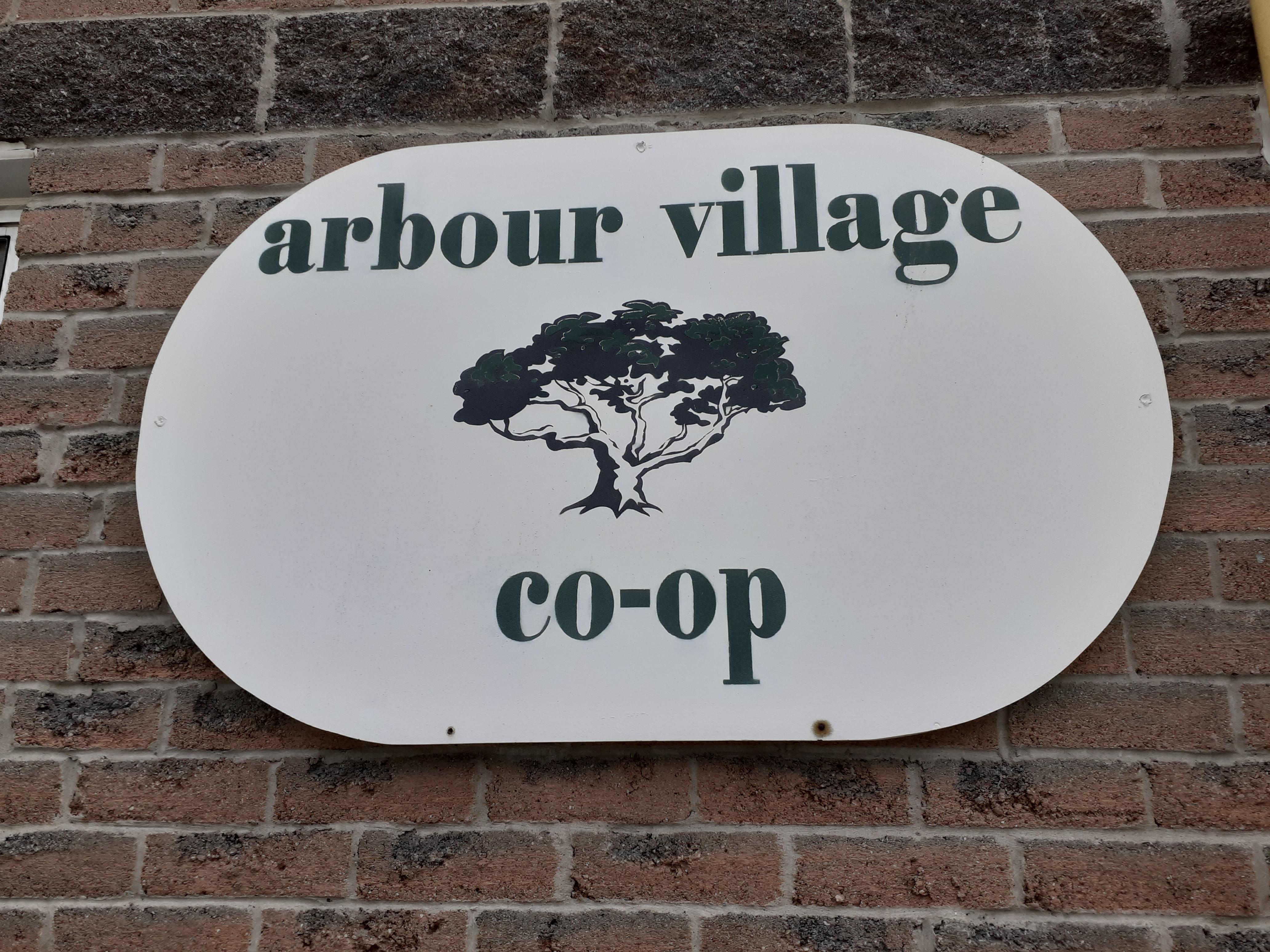 Arbour Village Coop written on a sign with an image of a tree on a brick wall w