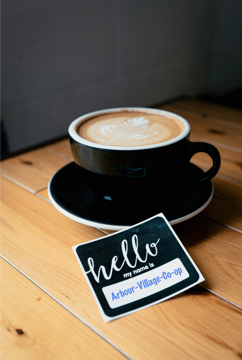 A coffee cup with a sticker beside it that reads Hello my name is Arbour Village Co-op